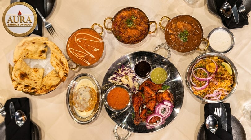 Overhead view of a table laden with various Indian dishes, including curries, naan, biryani, and tandoori chicken.