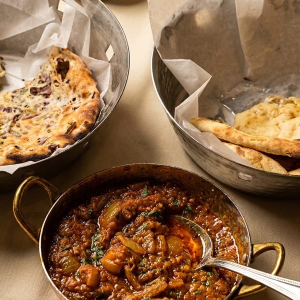 Indian meal with two baskets of naan bread and a bowl of curry with a spoon.
