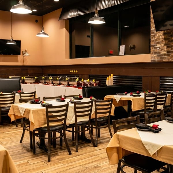 Restaurant dining room with tables set with red roses, a buffet line, and brick accent walls.