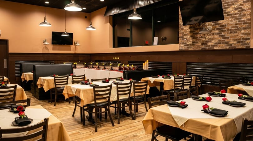 Restaurant dining room with tables set with red roses, black napkins, and a buffet line.