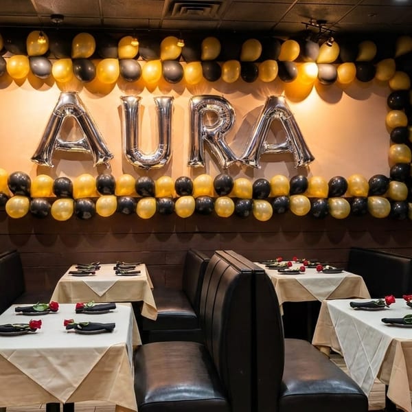 Restaurant interior with black booths, white tablecloths, red roses, and "AURA" balloons on the wall.