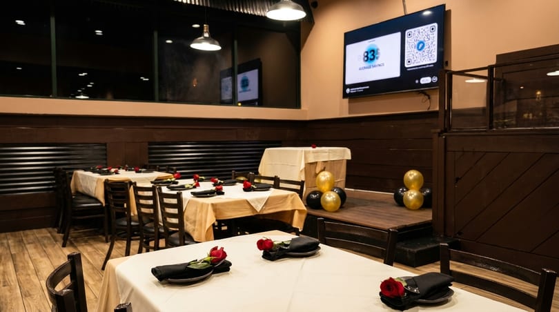 Restaurant dining room with tables set with white and tan tablecloths, black napkins, and red roses.