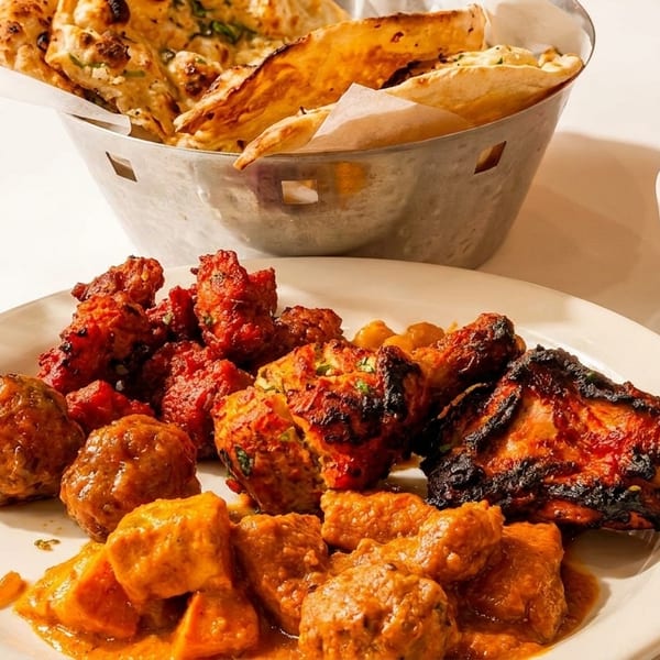 A plate of various Indian dishes including tandoori chicken, meatballs, and curry, with naan and sauce.