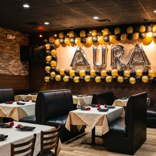 Restaurant dining room with black booths, white tablecloths, and a balloon display spelling "AURA".