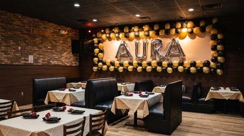 Restaurant dining room with black booths, white tablecloths, and a balloon display spelling "AURA".