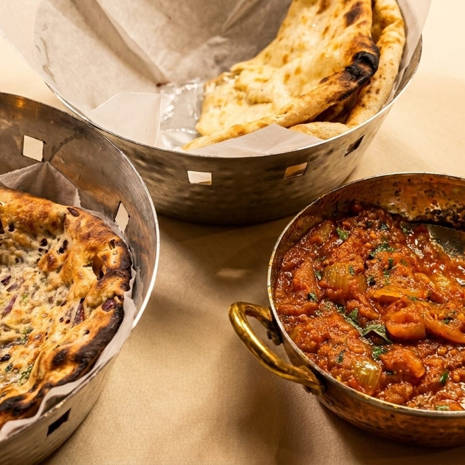 Indian food with two baskets of naan bread and a copper pot of curry on a tan tablecloth.