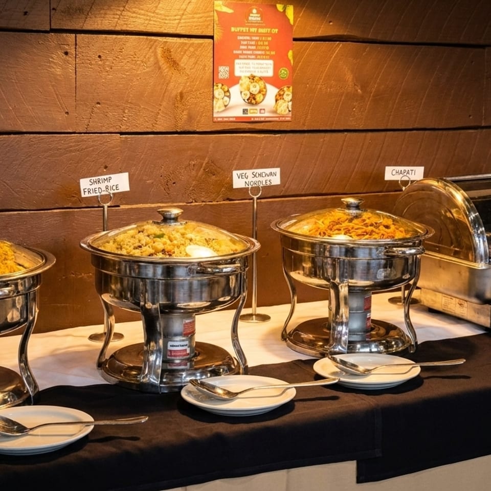 A buffet table with chafing dishes of Chicken Dum Biryani, Shrimp Fried Rice, and Veg Schezwan Noodles.