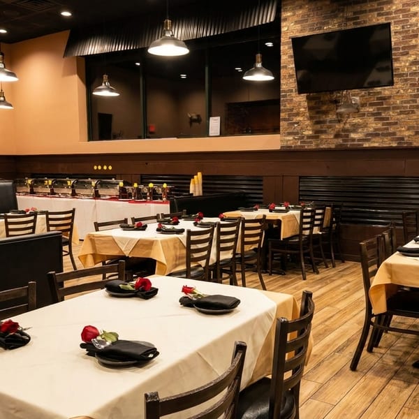 Restaurant dining room with set tables, booths, buffet line, and brick accent wall.
